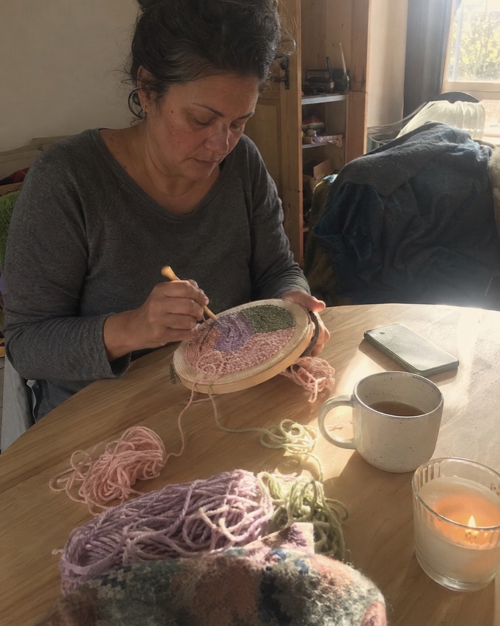 Woman doing punch needle at a table in the evening